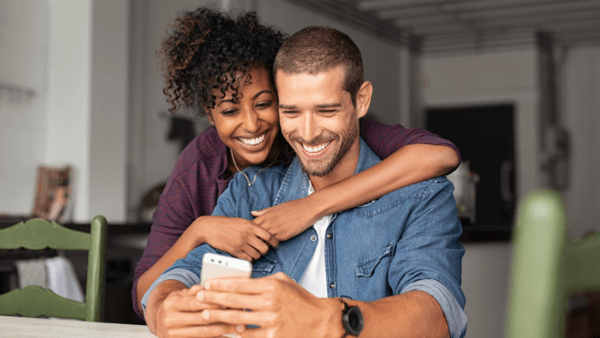 casal abraçado sorrindo olhando para celular