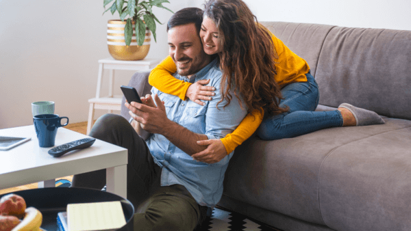 homem na sala de estar sendo abracado pela sua esposa